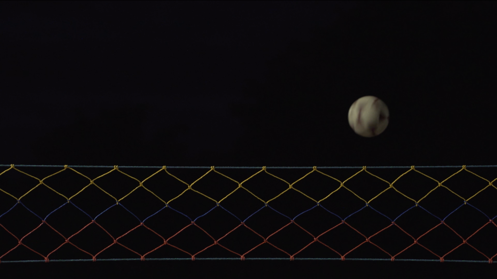 Nightime image of a volleyball net and ball mid-flight. It looks almost like the moon