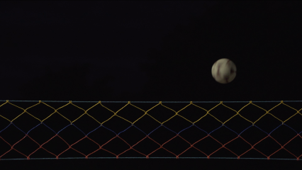 Nightime image of a volleyball net and ball mid-flight. It looks almost like the moon
