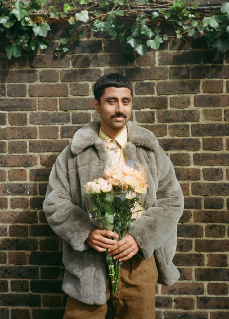 Portrait of a smiling Mohammed wearing a fur coat and carrying a bunch of roses